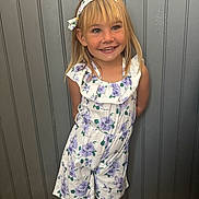 Olivia a rejoint le concours — aidez-le/la à gagner de superbes lots ! child, girl, smiling, blonde_hair, headband, floral_pattern, romper, standing, indoor, wall, grey_wall, happy, portrait, casual_clothing, young, cute, person, fashion, tile_floor, light