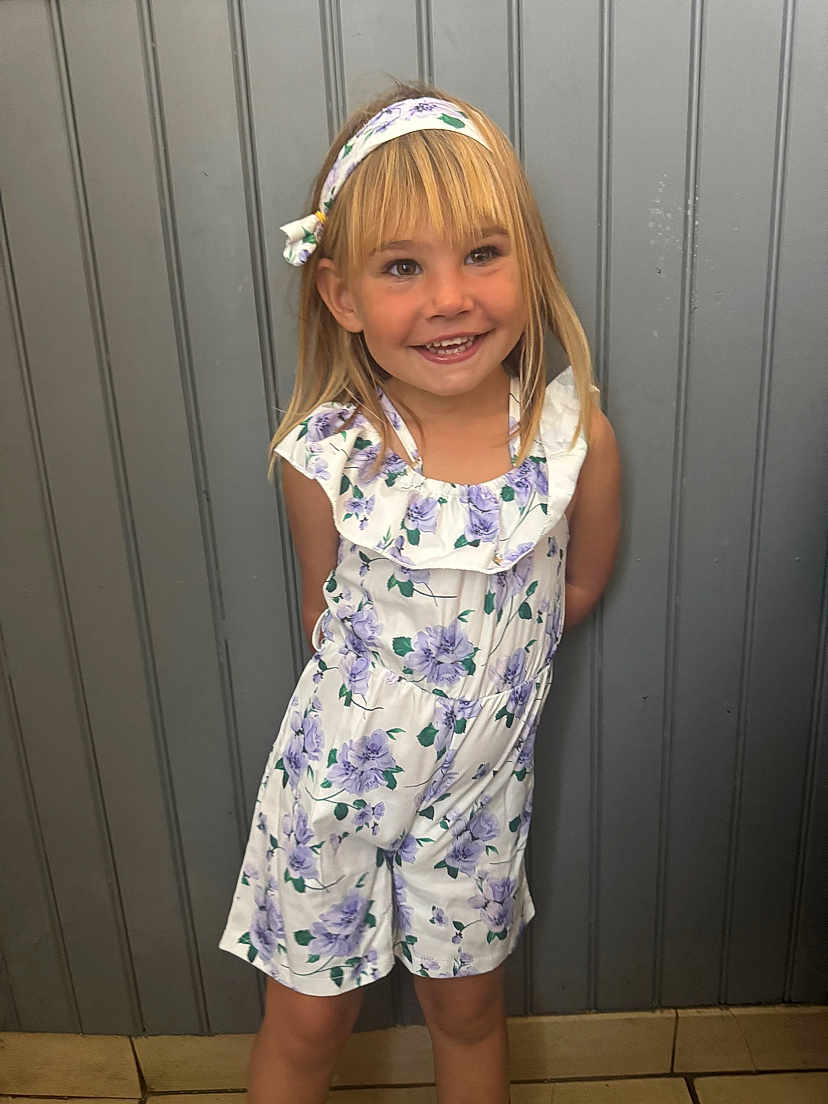 Olivia a rejoint le concours — aidez-le/la à gagner de superbes lots ! child, girl, smiling, blonde_hair, headband, floral_pattern, romper, standing, indoor, wall, grey_wall, happy, portrait, casual_clothing, young, cute, person, fashion, tile_floor, light