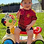 Lou a rejoint le concours — aidez-le/la à gagner de superbes lots ! toddler, child, toy, ride_on, zebra, outdoor, grass, cap, red_jersey, smiling, sunny, garden, play, summer, happy, plastic_toy, blue_shoes, green_wheel, background_blur, daylight