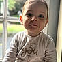 Lou a rejoint le concours — aidez-le/la à gagner de superbes lots ! toddler, child, window, natural_light, shirt, text_on_clothing, indoors, portrait, cute, baby, face, expression, hand, long_sleeve, young_child, person, casual_clothing, smiling, curious, soft_light