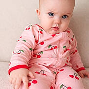 Everly is registered to the contest to win money with this photo: baby, child, infant, pink_clothing, cherry_pattern, onesie, blue_eyes, sitting, soft_texture, curious_expression, indoor, portrait, cute, young_child, fingertip, face, eyebrows, skin, person, closeup