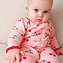 baby, child, infant, pink_clothing, cherry_pattern, onesie, blue_eyes, sitting, soft_texture, curious_expression, indoor, portrait, cute, young_child, fingertip, face, eyebrows, skin, person, closeup