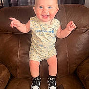 Leeland is registered to the contest to win money with this photo: baby, child, smile, happy, sitting, armchair, clothing, romper, sneakers, shoes, indoor, person, cute, blond_hair, blue_eyes, furniture, portrait, baby_clothes, feet, joy