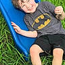 child, boy, smiling, slide, blue_slide, grass, outdoor, shorts, batman_tshirt, footwear, happy, play, summer, casual_clothing, greenery, fun, daylight, person, nature, grass_field