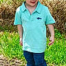 child, boy, cowboy_hat, outdoor, grass, jeans, boots, polo_shirt, smiling, sunny, fence, nature, casual_clothing, standing, young, portrait, greenery, happy, daylight, person