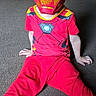 child, costume, iron_man, mask, red_clothing, carpet, indoor, superhero, sitting, furniture, dining_room, curious, eyes_visible, playful, home, floor, young_child, portrait, casual, bright_colors