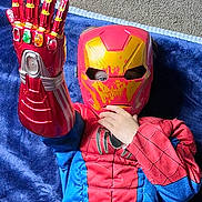 Benjamin Cash is registered to the contest to win money with this photo: blue_blanket, carpet, child, colorful, costume, eye, face, fingers, hand, indoor, infinity_gauntlet, iron_man, mask, play, pose, red, spiderman, superhero, toy, yellow