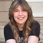 Aubree Elyse joined the competition — help win amazing prizes! person, smile, long_hair, wavy_hair, black_tshirt, outdoor, stairs, concrete, happy, young_person, casual, portrait, sitting, face, hair, light_skin, daylight, expression, teenager, front_view