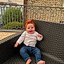 baby, child, smiling, outdoor, chair, woven_chair, headband, orange_headband, jeans, white_cardigan, barefoot, railing, stone_wall, building, sky, greenery, portrait, happy, cute, sitting