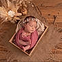 newborn, baby, sleeping, wooden_box, floral_headband, wrapped, burlap, dried_flowers, flower_arrangement, soft_cloth, peaceful, indoors, portrait, infant, cute, resting, natural_light, decor, wood_floor, cozy