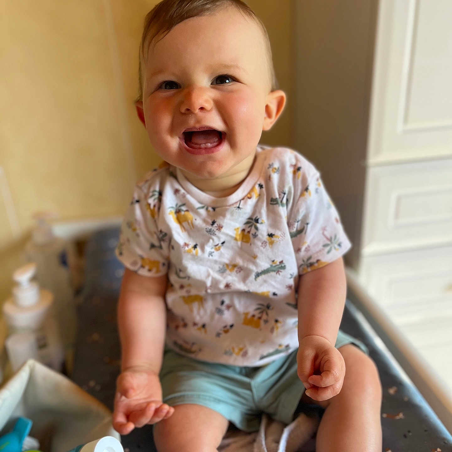 Manoa participe au concours pour gagner de l'argent avec cette photo : baby, bottle, cabinet, changing_table, child, clothing, face, furniture, hand, happy, indoor, infant, leg, room, shorts, skin, smile, toddler, toy, tshirt