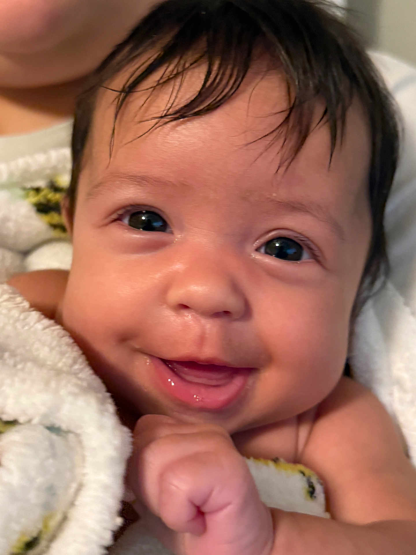 Sage is registered to the contest to win money with this photo: baby, close_up, smiling, face, towel, skin, infant, child, cute, portrait, happy, hand, dark_hair, indoors, expression, young, person, human, cheerful, wrapping