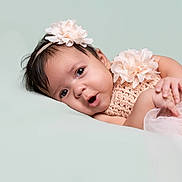 Sage is registered to the contest to win money with this photo: baby, infant, girl, face, flower, headband, crochet, pink, dress, tulle, soft, lying_down, portrait, cute, child, skin, hand, expression, closeup, background