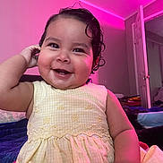 Mia is registered to the contest to win money with this photo: baby, cheerful, child, cozy, curly_hair, cute, face, happy, indoor, infant, lighting, open_door, person, pink_light, portrait, room, sitting, skin, smiling, yellow_dress