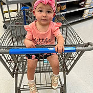 Ellie joined the competition — help win amazing prizes! toddler, child, shopping_cart, store_aisle, pink_headband, pink_shirt, shorts, sneakers, floor, metal, shelves, products, shopping, cute, curious, person, indoor, retail, baby, footwear