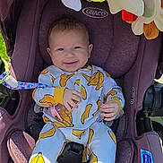 Adaline is registered to the contest to win money with this photo: baby, infant, car_seat, purple, banana_print, onesie, smiling, happy, child, toy, rainbow_toy, star_toy, green_ball_toy, seatbelt, outdoor, sunlight, graco, snugride_dlx, playful, cute