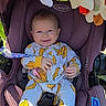 baby, infant, car_seat, purple, banana_print, onesie, smiling, happy, child, toy, rainbow_toy, star_toy, green_ball_toy, seatbelt, outdoor, sunlight, graco, snugride_dlx, playful, cute