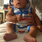 Jerome joined the competition — help win amazing prizes! baby, infant, child, person, clothing, hood, striped_clothing, feet, hand, bed, indoor, furniture, table, adult_hand, portrait, casual, cute, sitting, skin, face