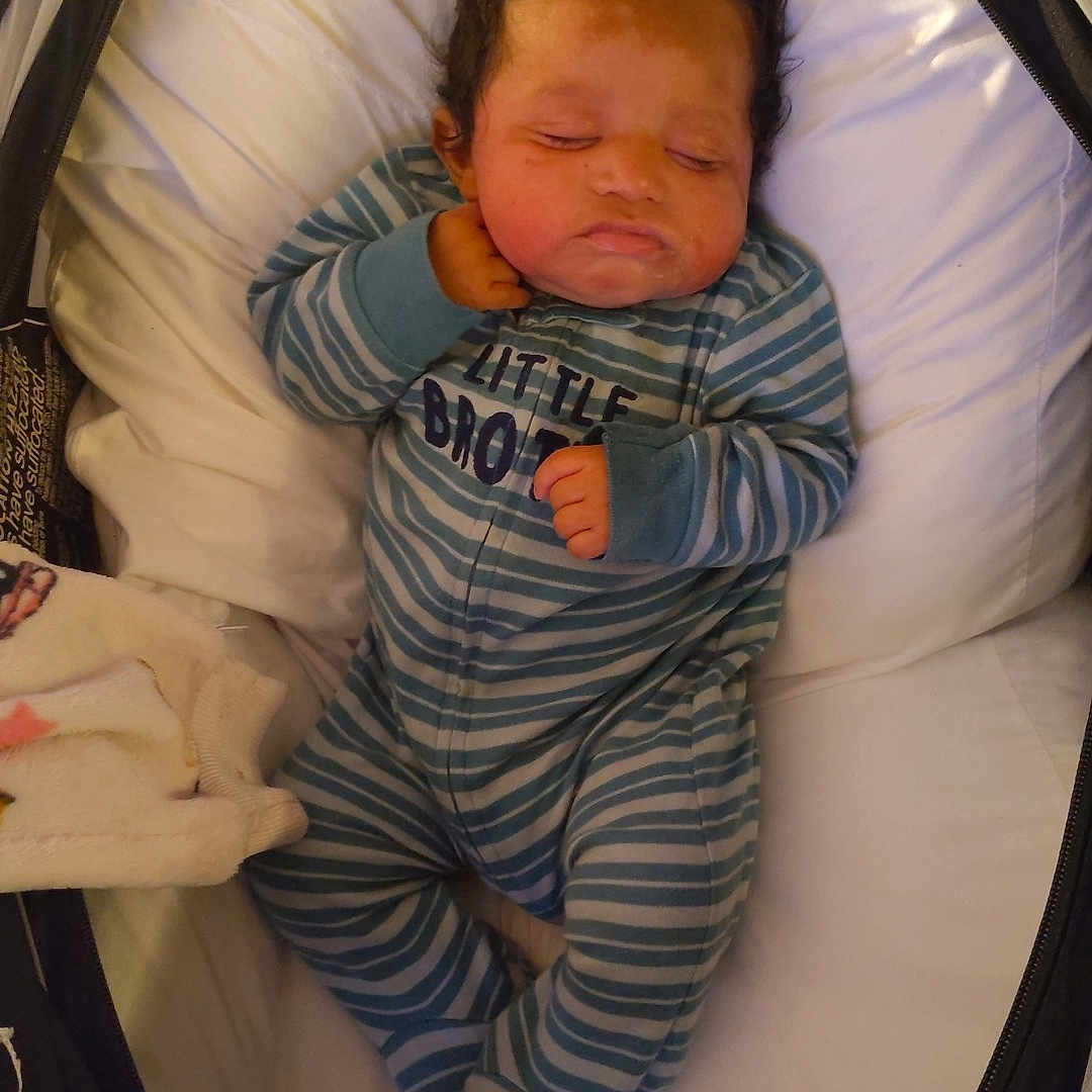 Jerome is registered to the contest to win money with this photo: baby, sleeping, infant, pajamas, striped_clothing, bassinet, cushion, cozy, indoor, child, newborn, cute, peaceful, resting, face, hand, footed_pajamas, soft, blanket, portrait