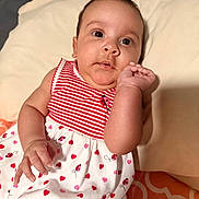 Kelsey is registered to the contest to win money with this photo: baby, infant, child, dress, pillow, red_stripes, ladybug_pattern, hearts, hand, face, eyes, skin, cute, lying_down, indoors, bed, blanket, curious, young, portrait