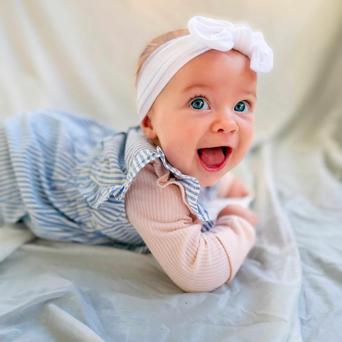 Riya joined the competition — help win amazing prizes! baby, child, smile, happy, blue_eyes, headband, bow, striped_dress, blanket, lying_down, cute, portrait, infant, soft_lighting, indoor, closeup, joyful, expression, face, person