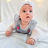 Riya joined the competition — help win amazing prizes! baby, infant, headband, blue_eyes, striped_clothing, white_blanket, lying_down, curious, soft_light, indoors, portrait, cute, child, small_hands, pink_sleeves, ribbons, closeup, face, expression, adorable