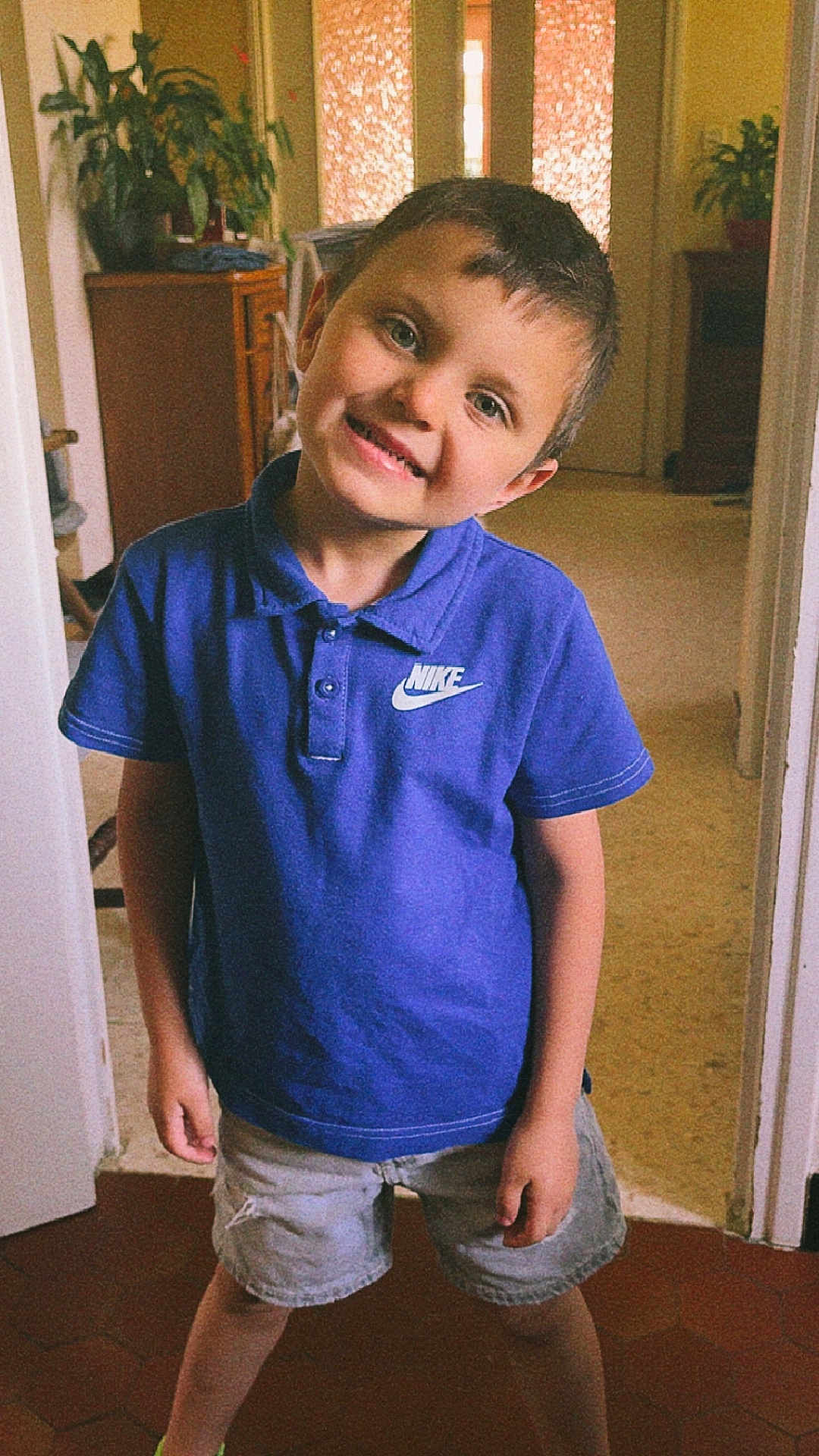 Ninyo a rejoint le concours — aidez-le/la à gagner de superbes lots ! child, boy, smiling, blue_shirt, nike, shorts, indoor, home, plant, furniture, door, floor, portrait, happy, casual_clothing, standing, head_tilt, person, young, cute