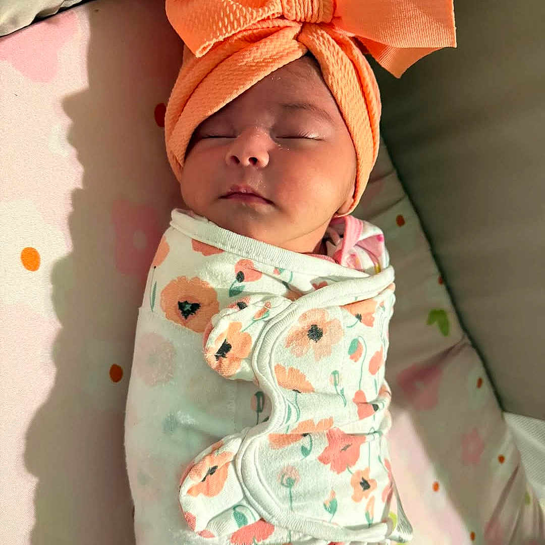 Isabella is registered to the contest to win money with this photo: adorable, baby, blanket, child, closeup, cute, face, floral, headband, indoors, infant, newborn, orange, peaceful, portrait, resting, sleeping, soft_light, swaddle, wrapped