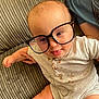 Elias is registered to the contest to win money with this photo: baby, glasses, couch, messy, tongue_out, infant, clothing, sitting, cute, chubby, playful, indoor, person, face, skin, hand, foot, texture, fabric, light
