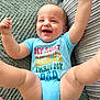 baby, infant, smiling, blue_onesie, text_on_clothing, happy, arms_up, legs_up, blanket, cushion, indoor, cute, child, playful, face, person, toddler, soft_texture, closeup, joyful