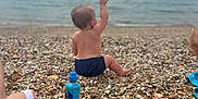 Atlas joined the competition — help win amazing prizes! toddler, child, beach, water, sea, pebbles, sitting, back_view, drink_bottle, sky, cloudy, person, foot, hand, shore, outdoor, relaxation, summer, nature, casual