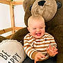 baby, child, smiling, drool, plush_bear, striped_sweater, pillow, text_on_pillow, wooden_frame, ivy, indoor, happy, cute, sitting, clothing, person, face, hand, toddler, cozy
