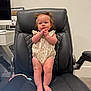 Adalyn is registered to the contest to win money with this photo: baby, child, infant, pigtails, black_leather_chair, office_chair, indoor, carpet, desk, computer_monitor, white_wall, clothing, barefoot, cute, person, furniture, portrait, hands_clasped, expression, home_office
