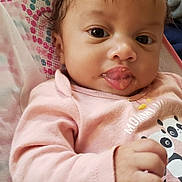 River joined the competition — help win amazing prizes! baby, infant, face, tongue, food, pink_clothing, panda_print, hand, blanket, patterned_blanket, curly_hair, lying_down, cute, child, indoors, closeup, expression, young_child, playful, messy_face