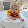baby, infant, headband, bow, yellow_dress, cushion, white_cushion, soft_toys, indoor, face, hands, curious, child, portrait, cozy, home, cute, light, soft_texture, comfortable
