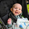 baby, child, infant, smiling, happy, stroller, blanket, portrait, outdoor, close_up, face, blue_eyes, laughing, seated, carriage, clothing, hand, baby_gear, soft_blanket, candid