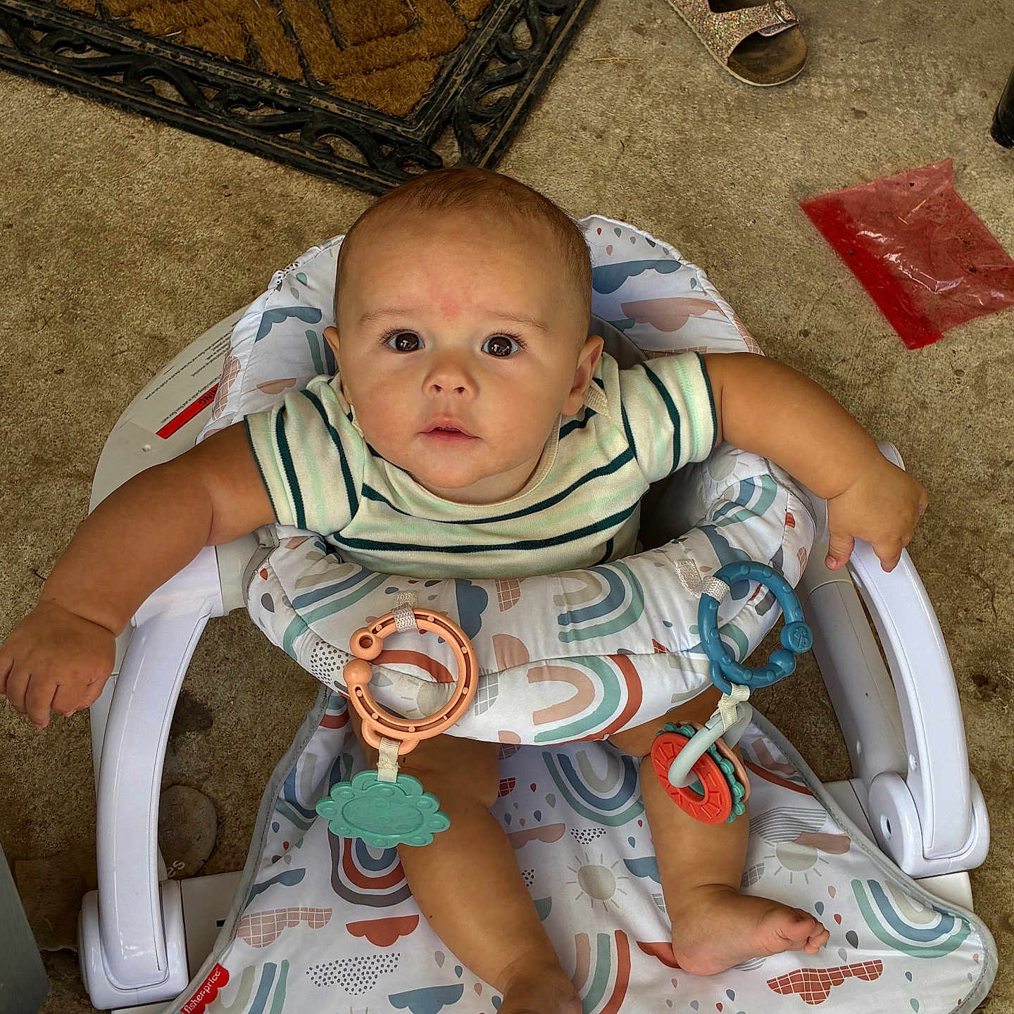 Weston joined the competition — help win amazing prizes! baby, child, infant, baby_seat, toys, striped_shirt, curious, indoors, floor, concrete, doormat, sandals, footwear, playful, looking_up, cute, small_hands, colorful, plastic_toys, seat