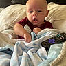 Weston joined the competition — help win amazing prizes! baby, bed, blanket, child, comfort, cozy, curious, cute, expression, hands, headboard, indoor, infant, maroon_shirt, person, pillow, remote_control, sleeping_area, soft_texture, young