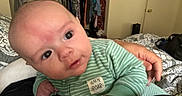 Weston joined the competition — help win amazing prizes! adult_hand, baby, bed, bedroom, blanket, closet, clothing, curious, door, expression, eyes, face, furniture, green_stripes, hand, indoor, infant, lying_down, onesie, person
