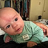 adult_hand, baby, bed, bedroom, blanket, closet, clothing, curious, door, expression, eyes, face, furniture, green_stripes, hand, indoor, infant, lying_down, onesie, person