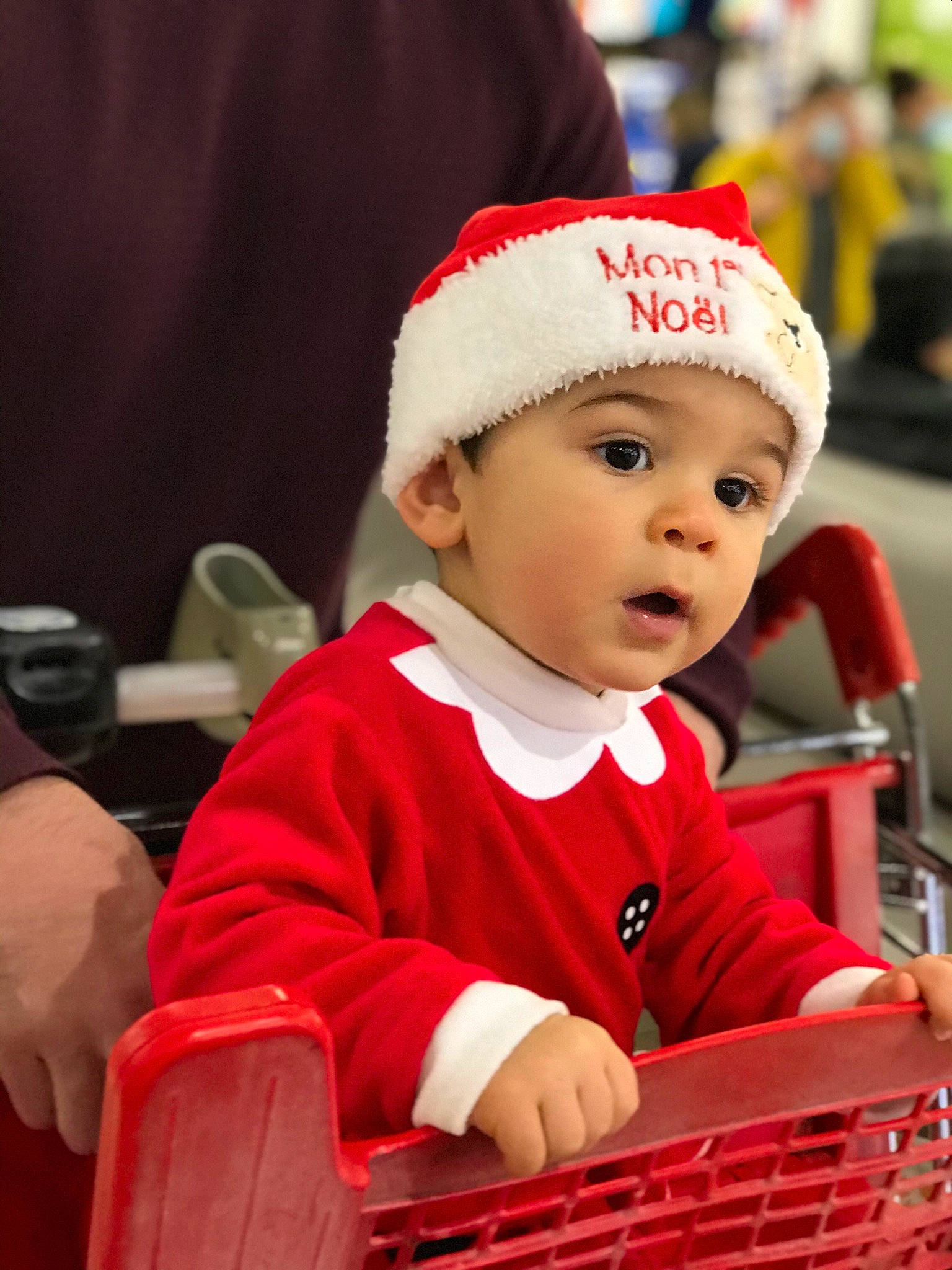 Tom a rejoint le concours — aidez-le/la à gagner de superbes lots ! baby, cap, carmine, child, christmas, christmas_eve, costume_hat, event, facial_expression, fictional_character, fun, happy, headwear, holiday, person, red, santa_claus, shopping_cart, sitting, surprise