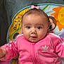 baby, child, pink_clothing, tracksuit, adorable, face, big_eyes, playmat, indoor, cute, infant, smiling, colorful, toy, young_child, head, hair_bow, sitting, person, portrait