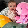 Ilyana a rejoint le concours — aidez-le/la à gagner de superbes lots ! baby, child, smiling, plush_toy, pink, cushion, fabric, indoor, happy, cute, person, face, clothing, soft_toy, seated, cozy, infant, playful, home, comfort