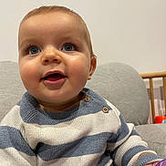 Mylann participe au concours pour gagner de l'argent avec cette photo : baby, child, smiling, blue_eyes, striped_sweater, sitting, indoor, couch, toy, happy, face, person, cute, infant, close_up, hand, clothing, furniture, home, portrait