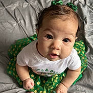 Xela is registered to the contest to win money with this photo: baby, bedspread, big_eyes, blanket, child, closeup, cute, feet, green_bows, green_skirt, hair, hands, indoors, infant, looking_up, playful, portrait, skin, smiling, white_shirt