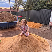 Aurora joined the competition — help win amazing prizes! child, smiling, outdoor, pile, sawdust, wood_shavings, backyard, fence, tree, dumpster, sunset, clothing, person, playful, ground, nature, garden, dirt, happy, curly_hair