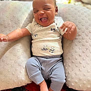 Jakai Kyrie is registered to the contest to win money with this photo: baby, infant, smiling, laughing, pajamas, pillow, blanket, soft_texture, indoor, child, cute, comfort, happy, face, foot, hand, pattern, red, black, cozy