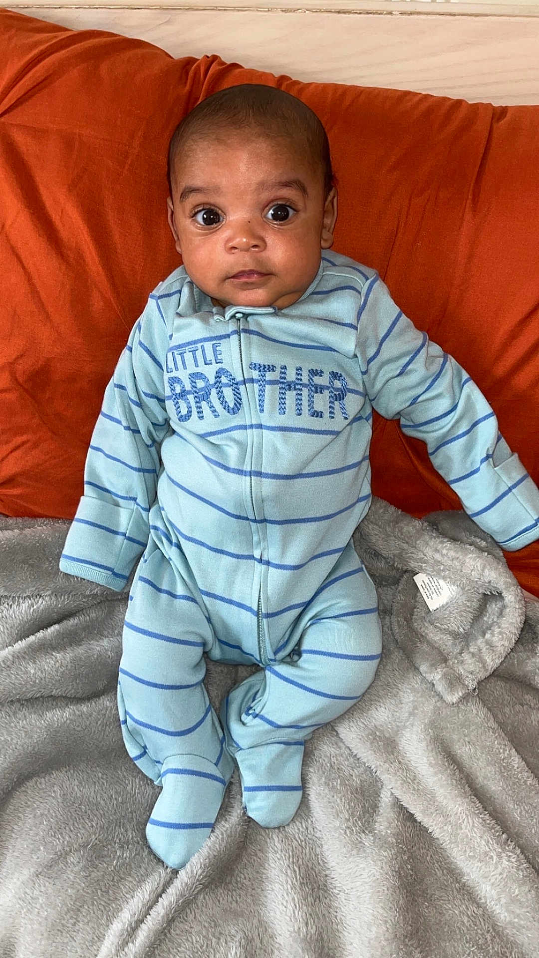 Jakai Kyrie is registered to the contest to win money with this photo: baby, child, infant, onesie, blue, striped_clothing, blanket, pillow, orange, face, wide_eyes, lying_down, cozy, soft_texture, indoor, cute, portrait, person, sleepwear, young