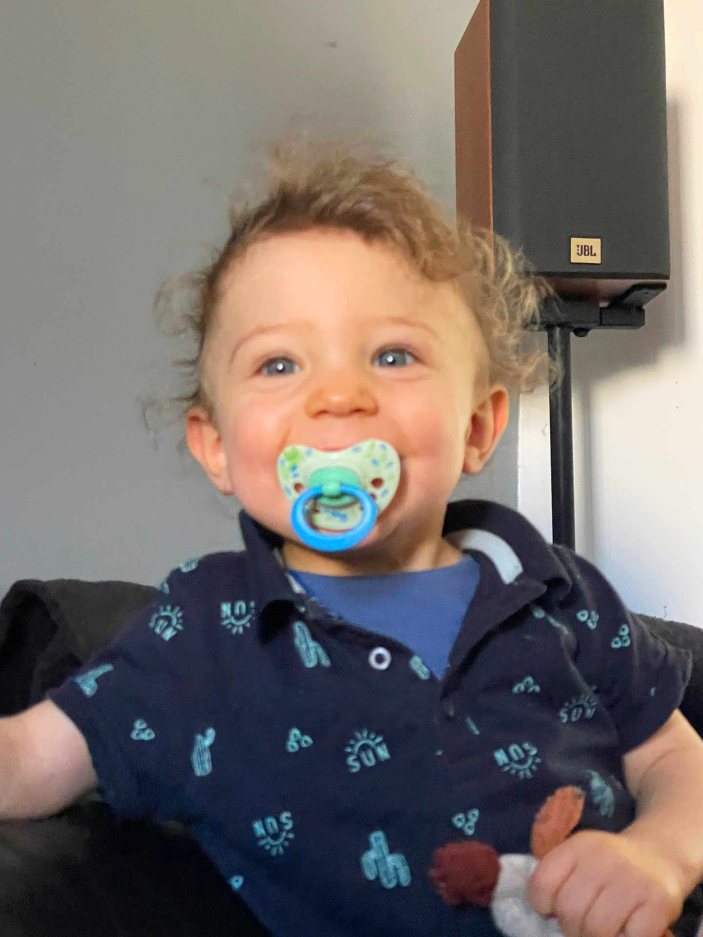 Elyoth participe au concours pour gagner de l'argent avec cette photo : blue_eyes, casual, child, comfort, couch, curly_hair, face, happy, home, indoor, navy_blue, pacifier, person, portrait, shirt, smiling, speaker, toddler, toy, young