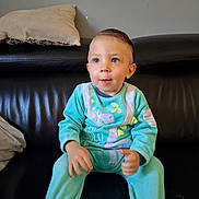 Elyoth participe au concours pour gagner de l'argent avec cette photo : baby, black_leather_couch, blue_eyes, casual, child, cozy_clothing, cute, dinosaur_onesie, furniture, happy, home, indoor, person, pillow, portrait, short_hair, sitting, smile, toddler, young_child